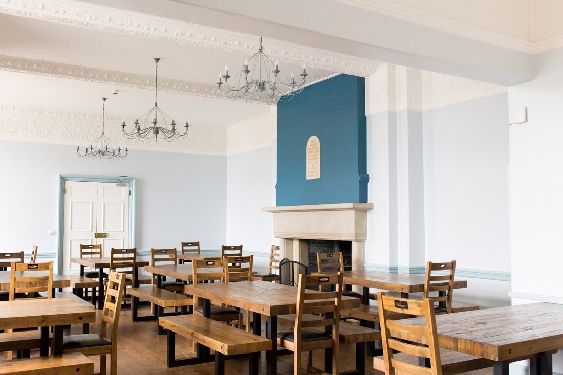 Dining room at Avon Tyrrell with wooden benches and tables as well as large open fire place