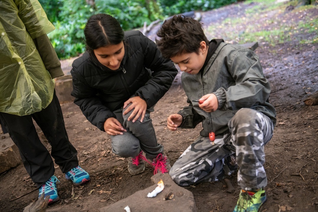 Two people knelt on the floor trying to light cotton wool with flint and steel on bushcraft