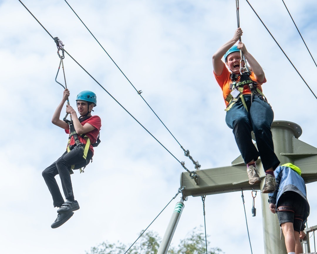 Two poeple on a zip line zipping through trees in the air with blue skies