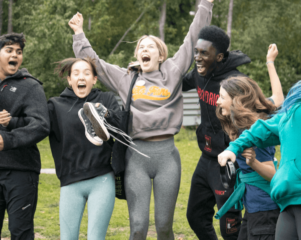 Group of young people smiling and cheering with arms in air in the forest at avon tyrrell outdoor centre