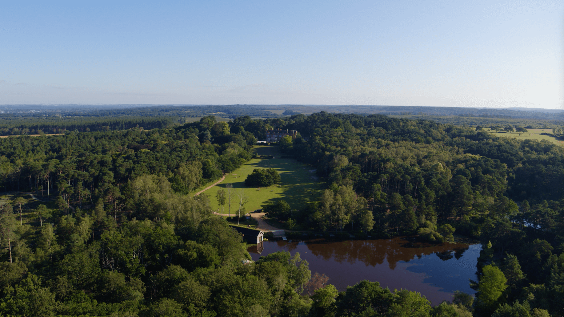 Drone shot of Avon Tyrrell Outdoor Centre in the new forest - lots of trees and lake in the foreground with manor house peeping through the trees
