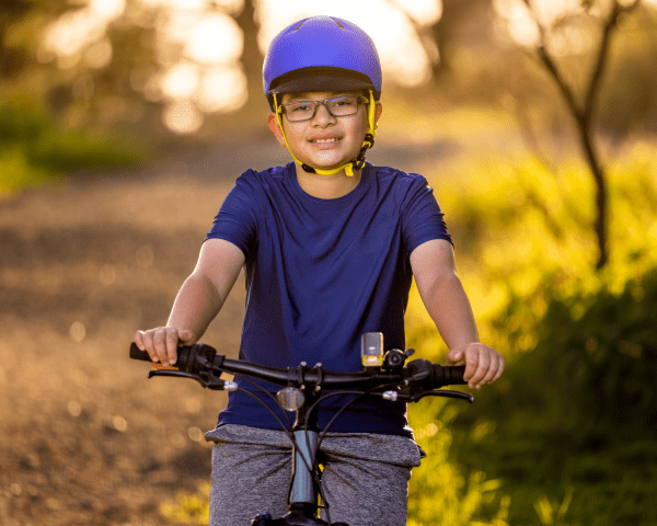 Young boy wearing helmet on a bike in a forest area smiling to camera