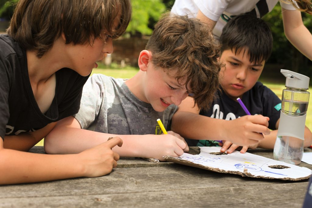 Boys around a table drawing and making bottle rocket out of cardboard