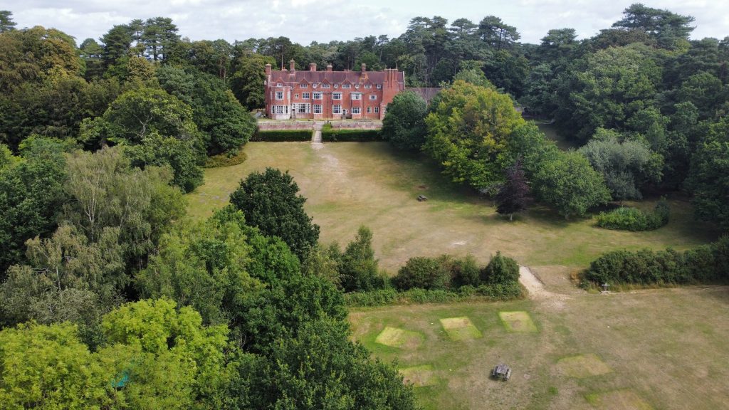 Avon Tyrrell Manor House in the New Forest National Park with trees and grass surrounding building drone image