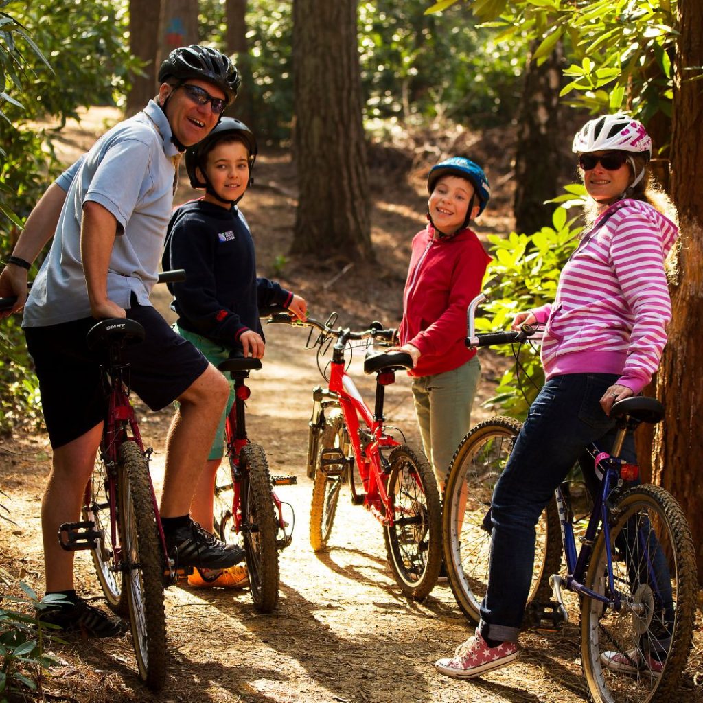 family on bikes with mum and dad smiling and two boys miling behind them ready for a bike ride in the forest wearing helmets