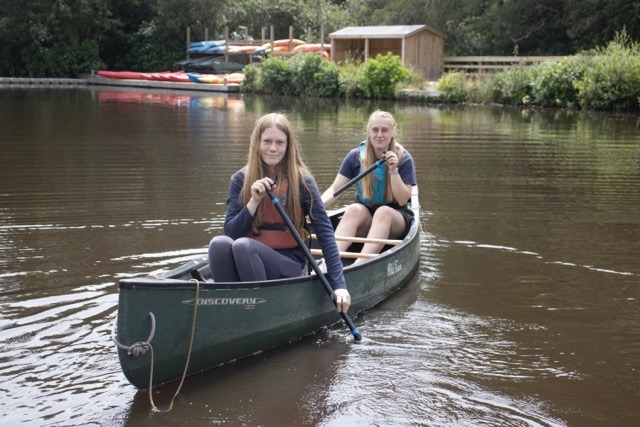 Young person and instructor wearing life jackets in a canoe on a lake in the forest smiling to camera