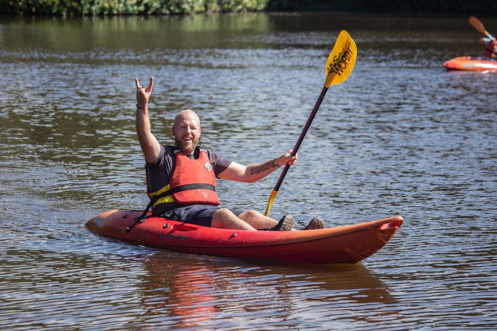 Man in kayak with paddle smiling to camera with rock fingers in air