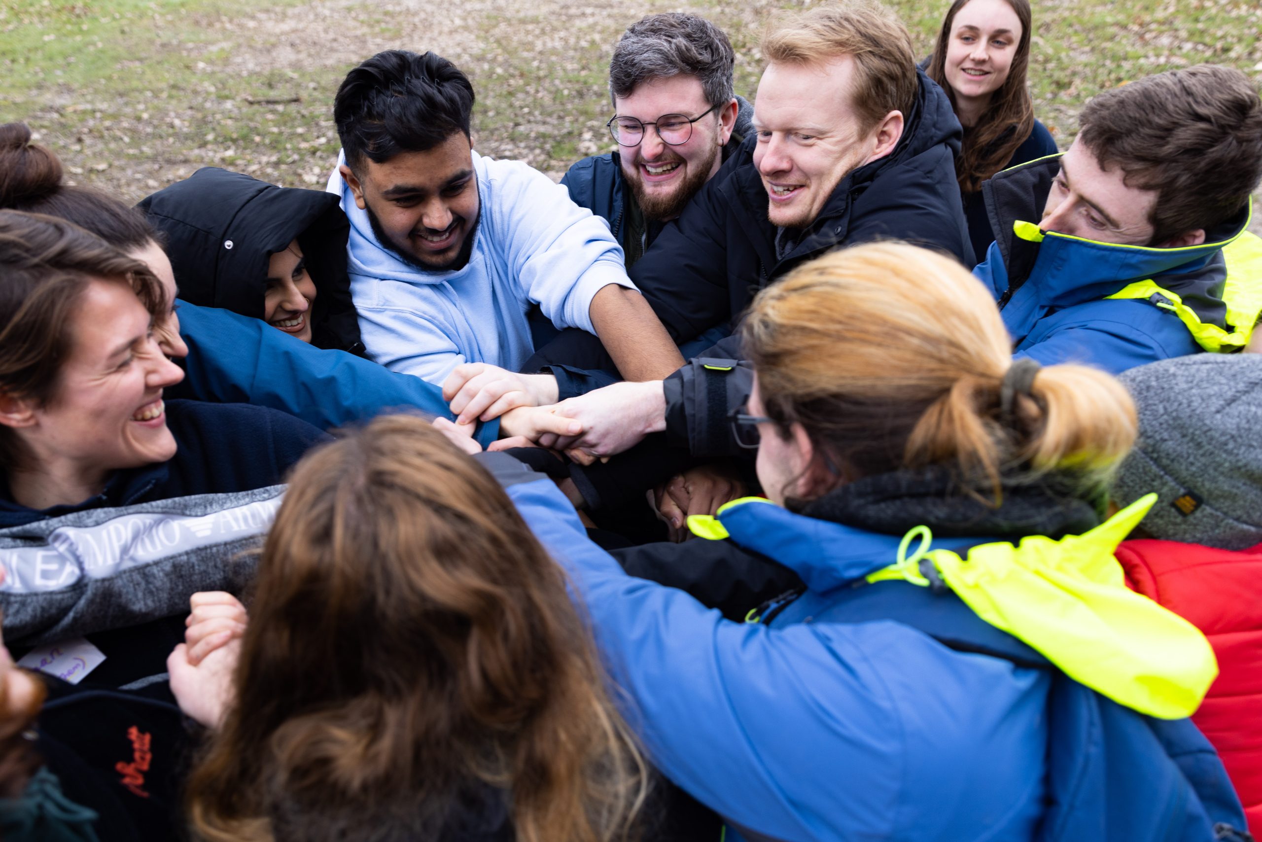 Group with hands in and on top of each other smiling in a team building exercise on a grass field