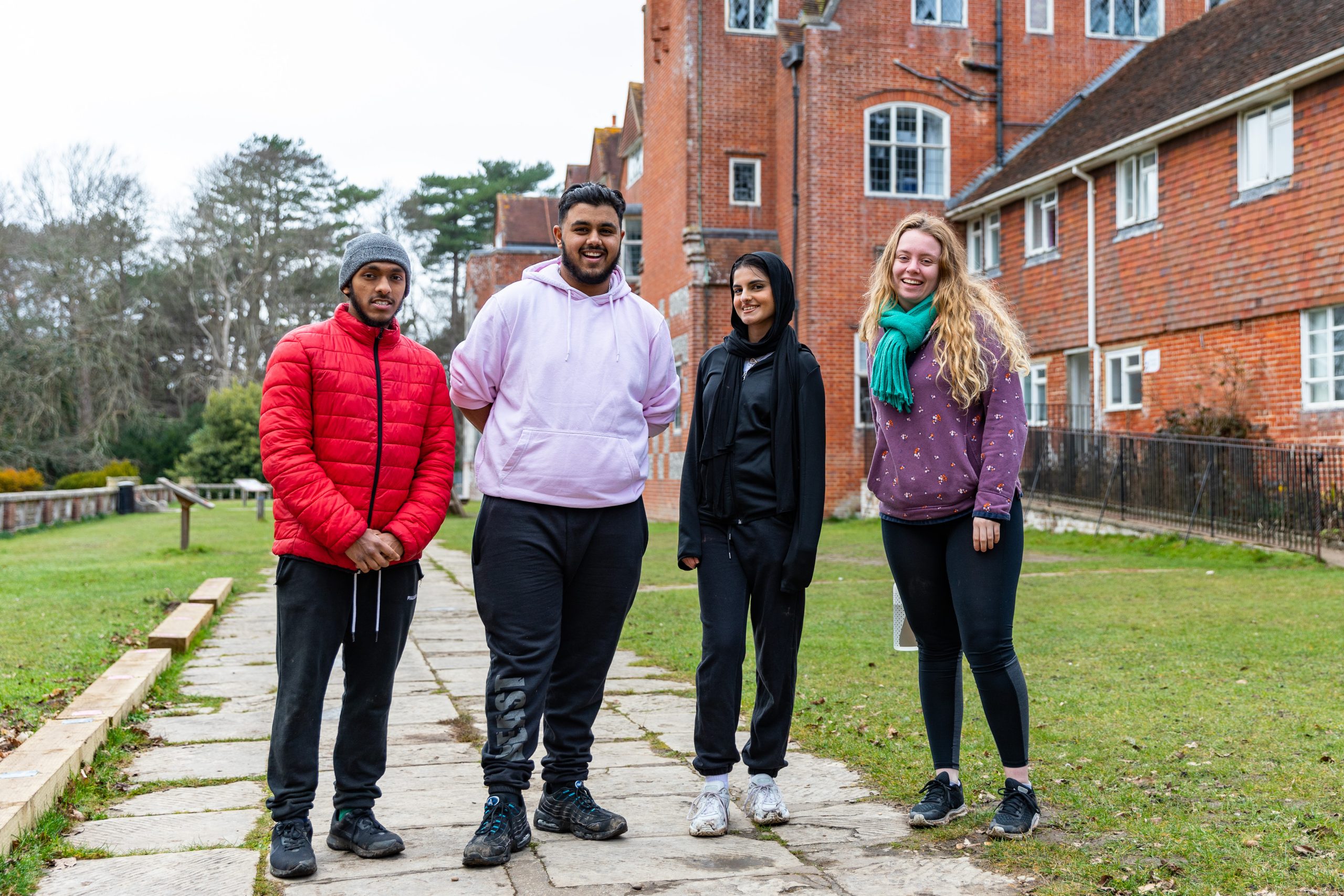 Four young adults stood together on a paved path in front of Avon Tyrrell's manor house in the new forest