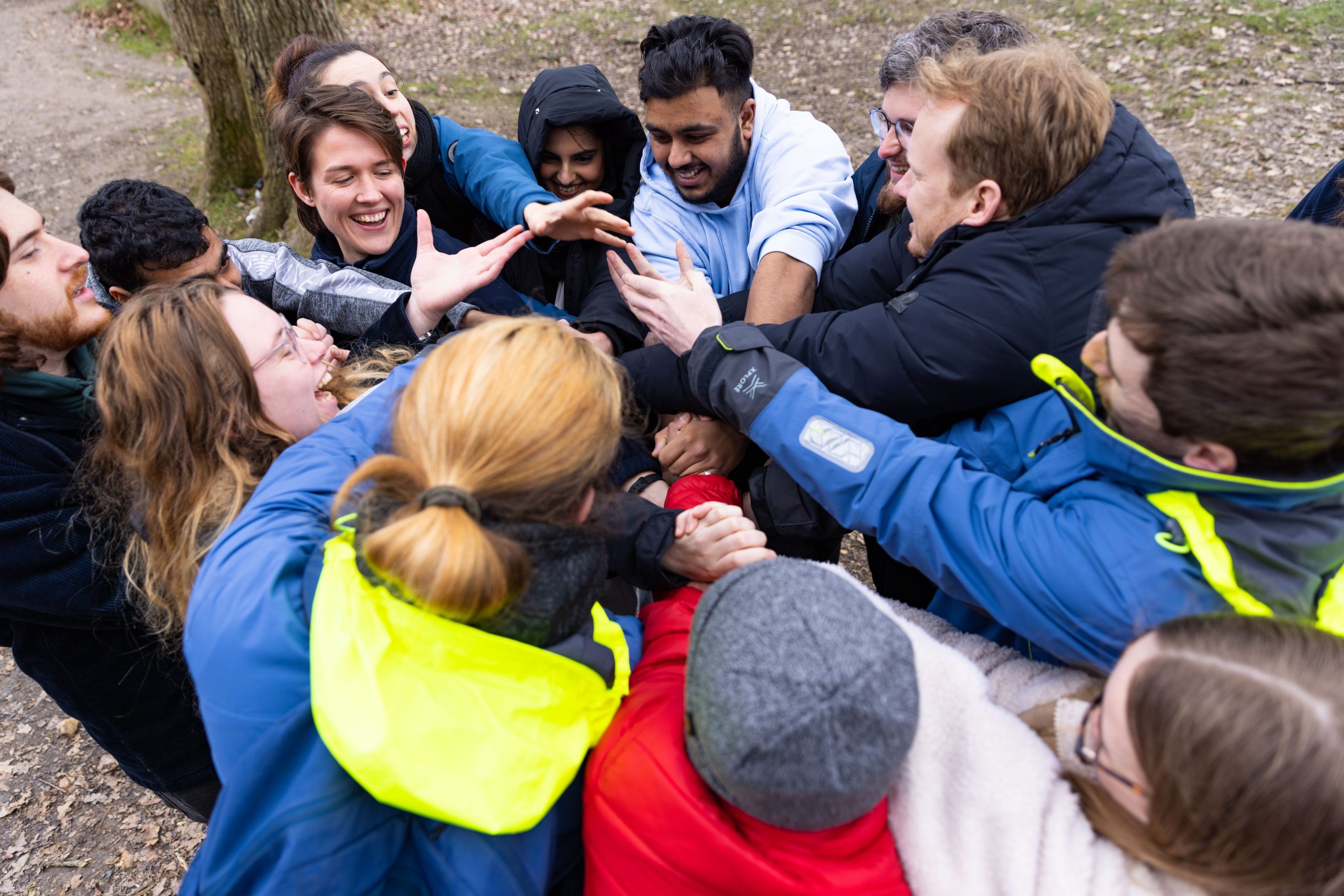 People with outstretched arms huddled in circle reaching for others hands in team building exercise at Avon Tyrrell Outdoor Centre