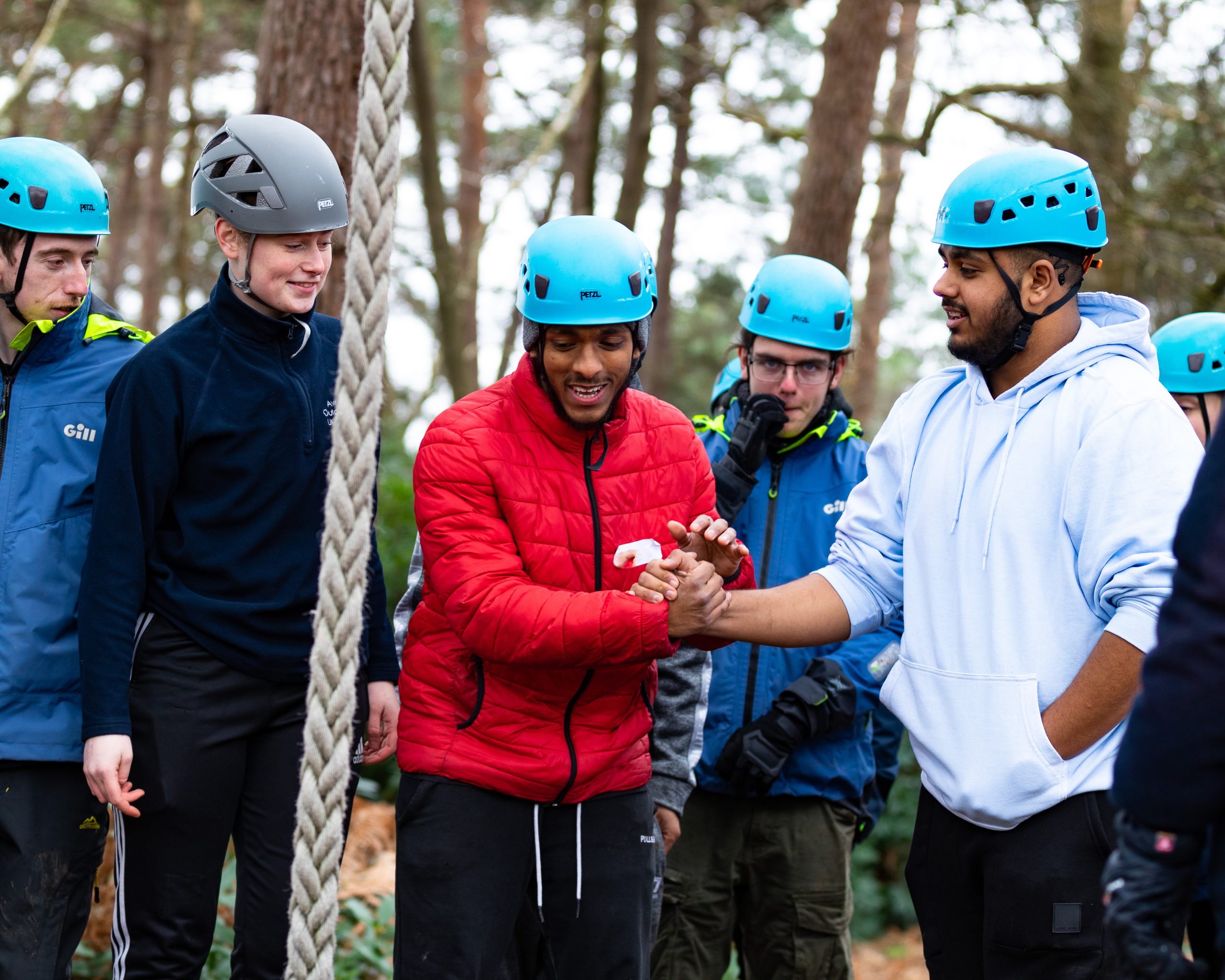 Young people wearing blue helmets taking part in low ropes with rope dangling close to camera