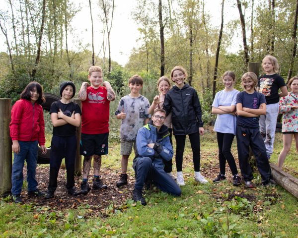 Group of young people siming to camera stood in a straight line with instructor sat in front posing. Image was taken in the New Forest with trees in the background on a winters day