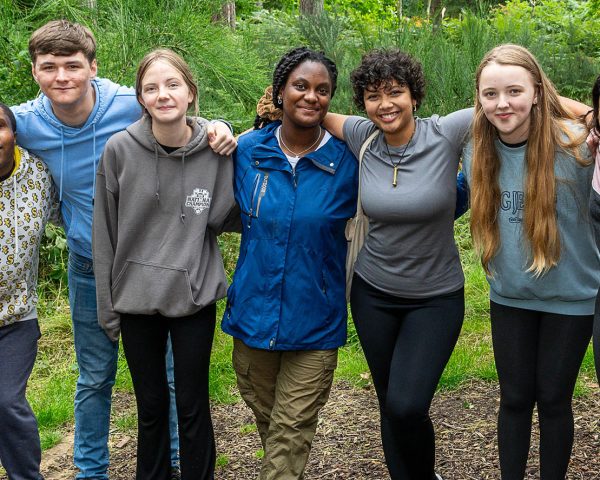 Group of young people stood in the forest with arms around each others shoulders smiling to camera