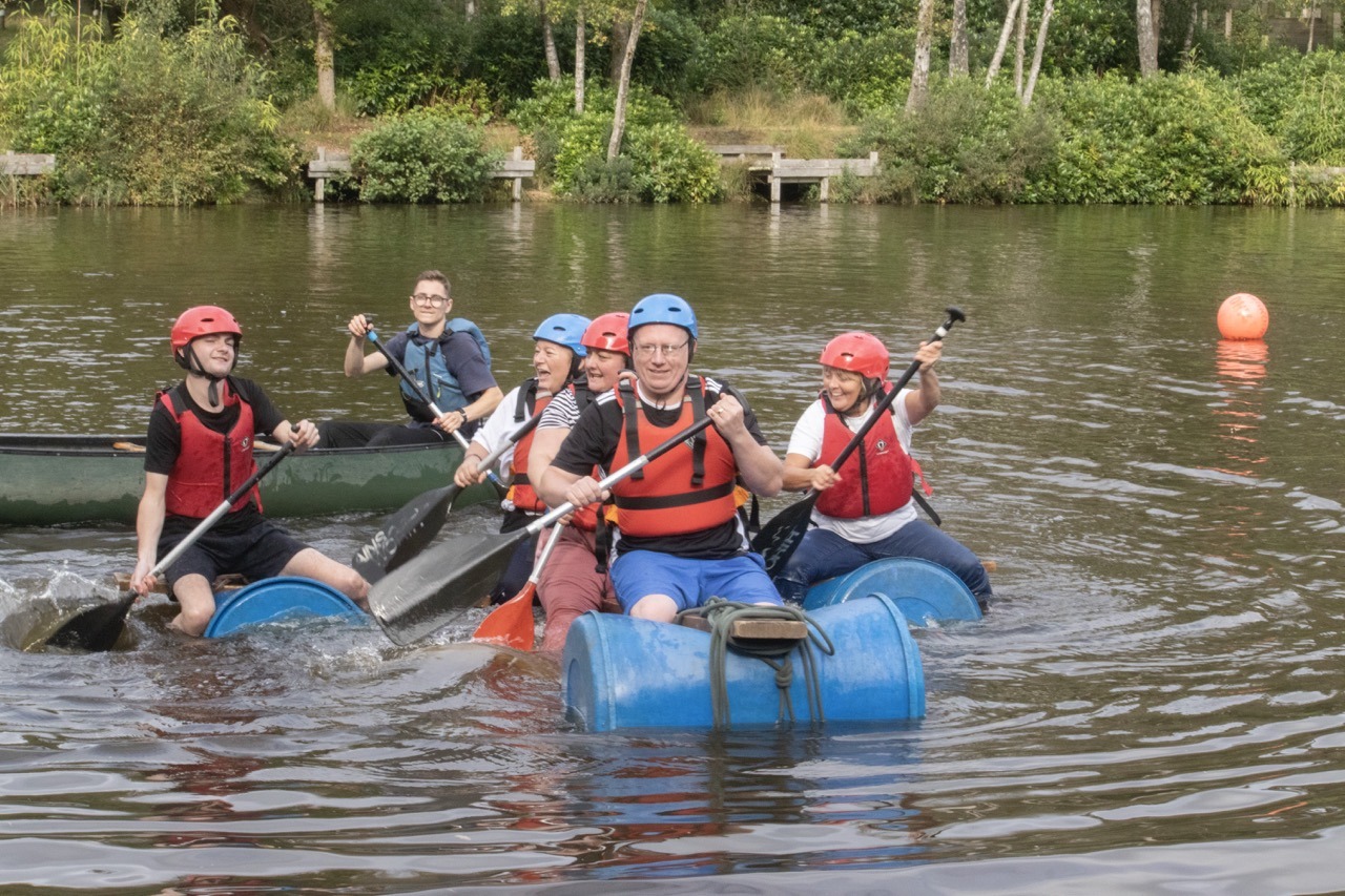 adult corporate group on raft in a lake paddleing towards camera